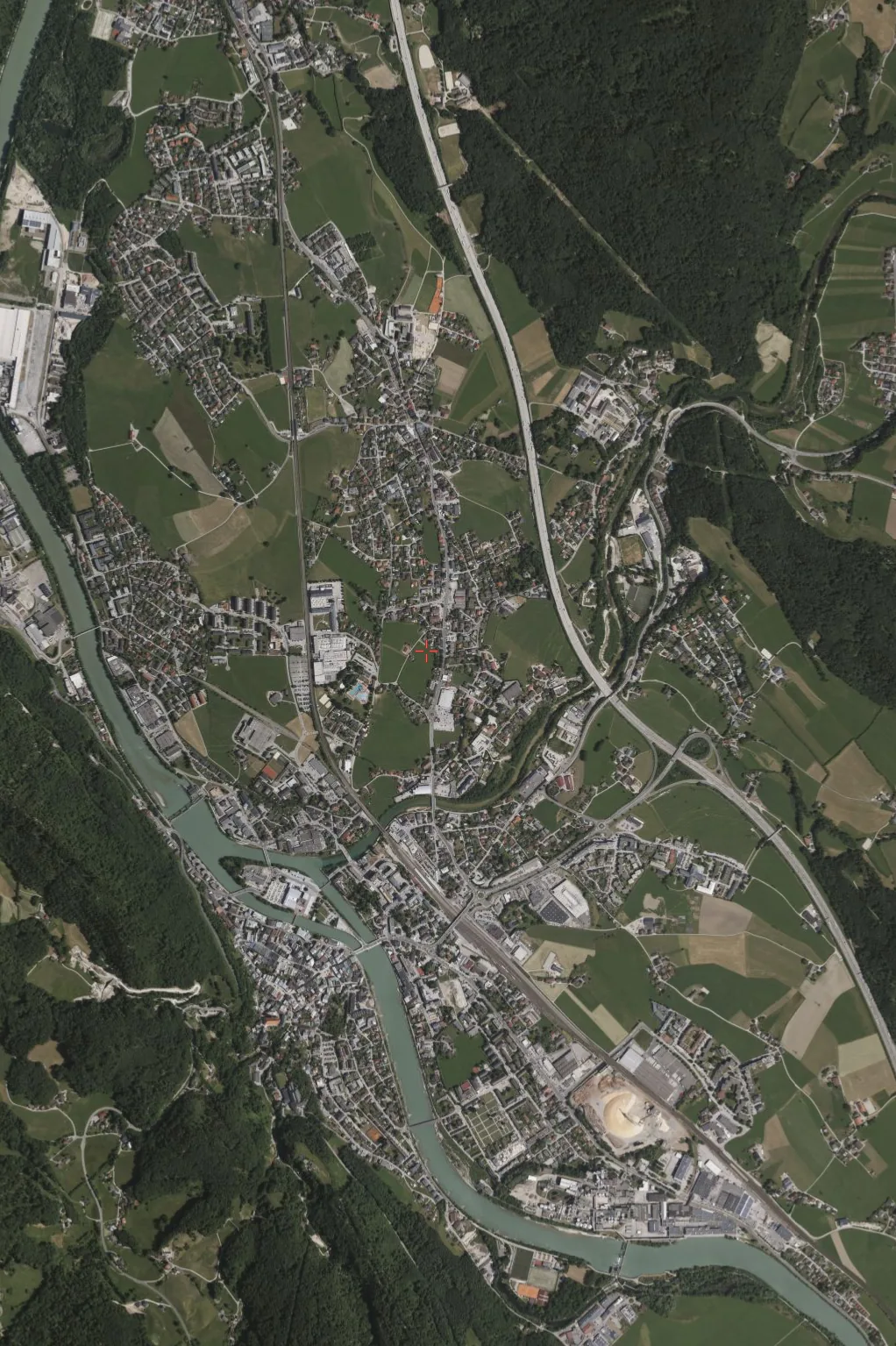 Aerial view of Hallein, Austria: roofs, roads and industrial sites next to fields, forest and the Salzach river.